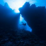 a person scubas through the water near a rock formation